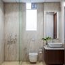 Beige Bathroom Design With Glass Partition, Wooden Vanity Unit And White Countertop - Livspace