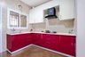 L shaped red and white kitchen with beige wall tiles - Livspace
